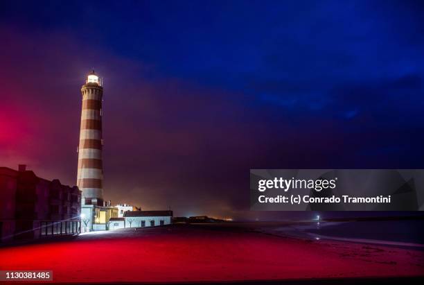 o farol de aveiro brilha sobre a praia de portugal iluminada pela luz vermelhoa do luminoso - orientação stock-fotos und bilder