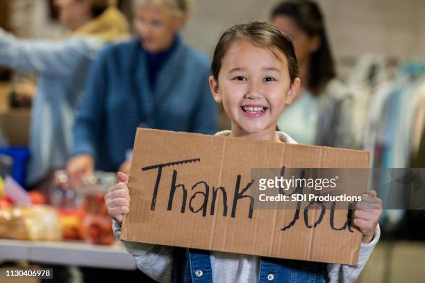 adorable young food bank volunteer holds 'thank you' sign - foundation for kids stock pictures, royalty-free photos & images