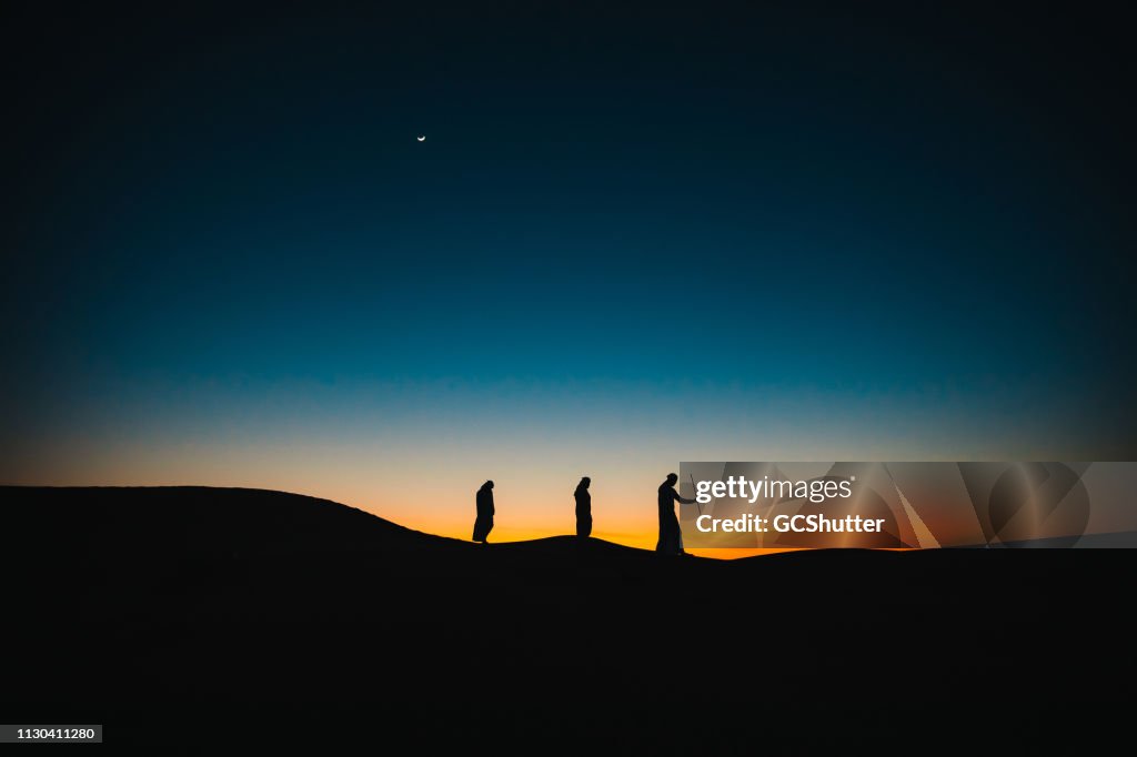 Arabs on the sand dunes walking behind each other during twilight