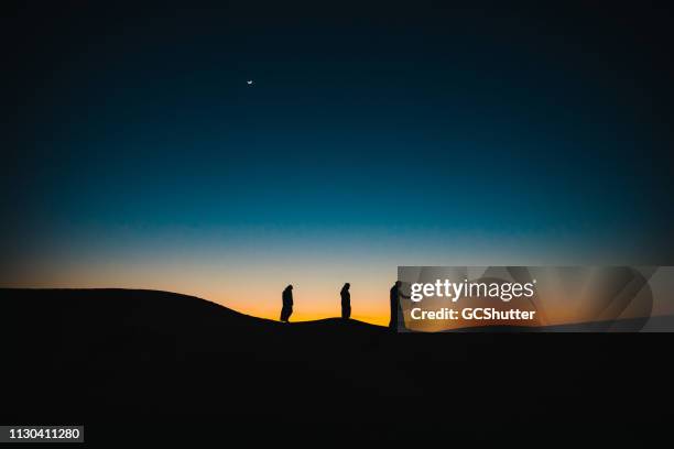 arabs on the sand dunes walking behind each other during twilight - ramadan dubai stock pictures, royalty-free photos & images