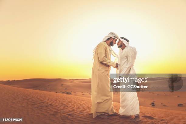 two arab men greeting each other on the sand dunes - ramadan greeting stock pictures, royalty-free photos & images