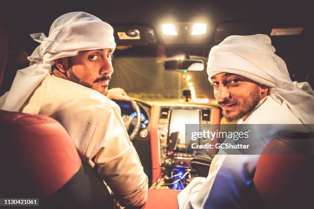 arab friends turning back while seated on the front seats of a suv - middle east cool stock pictures, royalty-free photos & images