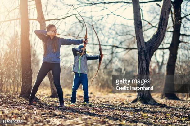 children practicing shooting bows in forest - bow hunting stock pictures, royalty-free photos & images