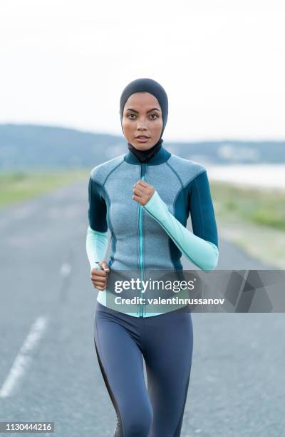 asian sportswoman with hijab jogging on the road - arab culture stock pictures, royalty-free photos & images