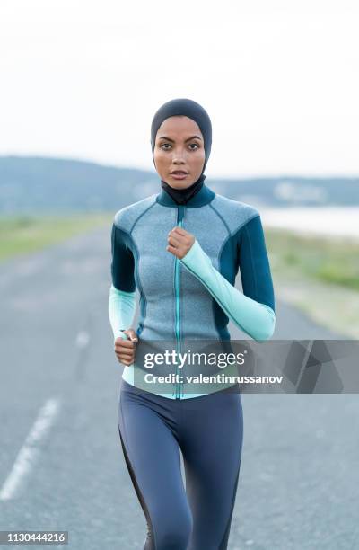 asian sportswoman with hijab jogging on the road - muslim woman beach stock pictures, royalty-free photos & images