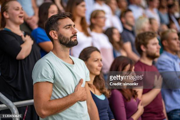 spectators singing national anthem in stadium - hands on chest stock pictures, royalty-free photos & images