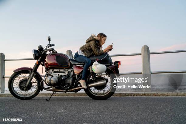 young girl texting sitting back to front on vintage motorcycle - biker photos et images de collection
