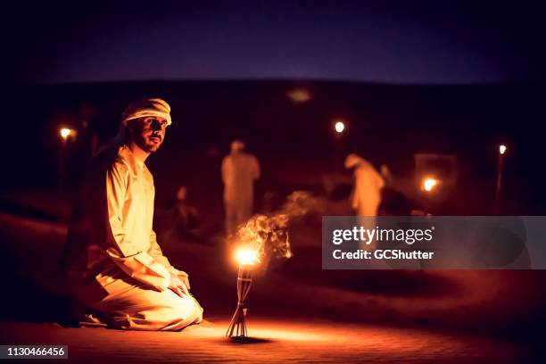 arab mean seated on the sand dunes near an oil lamp at a camp site - desert night stock-fotos und bilder