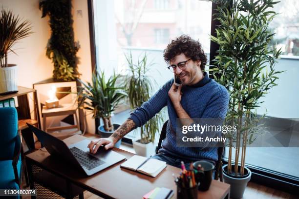 young man talking on the phone in his home office - voip stock pictures, royalty-free photos & images