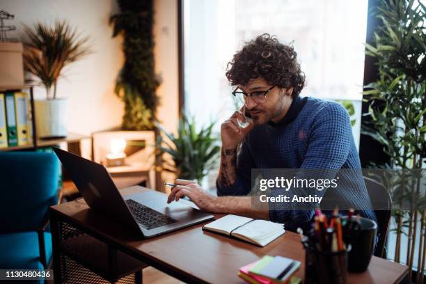 young man talking on the phone in his home office - trabalhar em casa imagens e fotografias de stock
