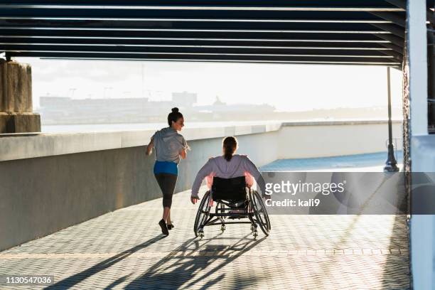 young woman with spina bifida, hispanic friend jogging - wheelchair stock pictures, royalty-free photos & images