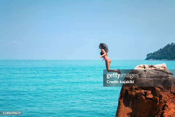 young woman on summer vacations jumping from cliff and diving into blue sea - cliff diving stock pictures, royalty-free photos & images