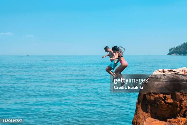 familie genieten op de zomervakantie, ze springen van de klif in de blauwe zee - girl diving stockfoto's en -beelden