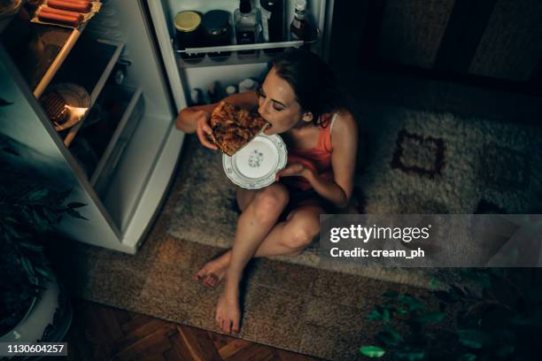 woman eating pizza slice in front of the refrigerator - eating disorder stock pictures, royalty-free photos & images
