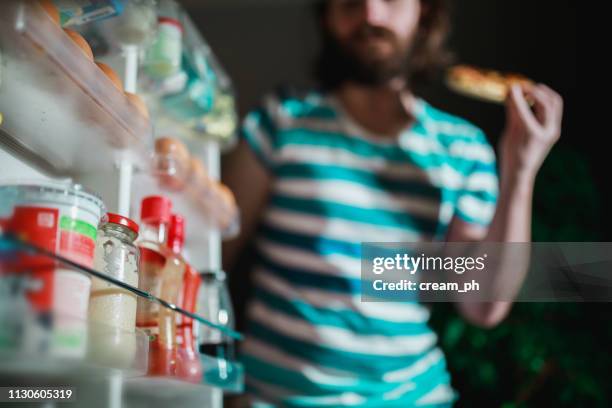 el hombre comiendo frente a la nevera tarde en la noche - trastorno de alimentación fotografías e imágenes de stock