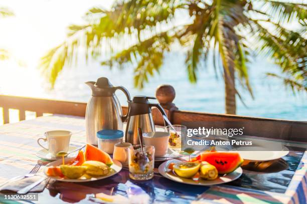 tropical breakfast with fresh fruit, tea and curd on the background of palm trees and the ocean - buffet fond stock-fotos und bilder