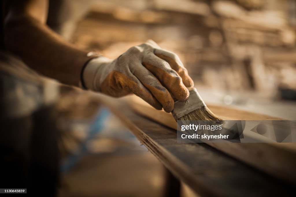 Close-up van Carpenter met behulp van borstel, terwijl de toepassing van beschermende vernis op een stuk hout.
