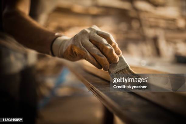 close up of carpenter using brush while applying protective varnish to a piece of wood. - overhaul stock pictures, royalty-free photos & images