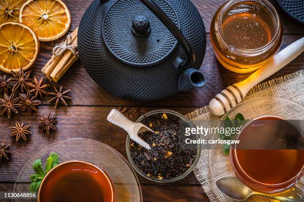 teezeit: tasse tee, zimtstangen, anis, getrocknete orange auf holztisch - ayurveda stock-fotos und bilder