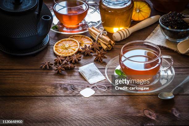 teezeit: tasse tee, zimtstangen, anis, getrocknete orange auf holztisch - tee stock-fotos und bilder