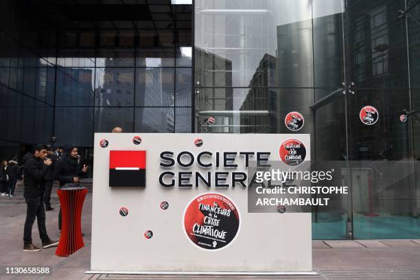 People stand near stickers reading "climate crisis' financers" outside the building of the Societe Generale bank headquarters in La Defense business...