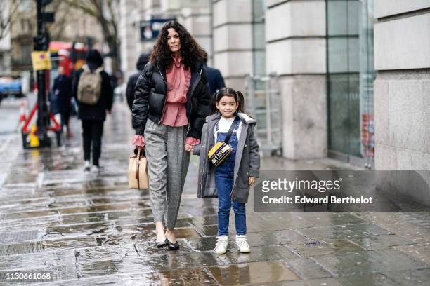 Hedvig Opshaug wears a black puffer jacket, a pink shirt, gray pants, a bag, black shoes ; her daughter wears a gray coat, a shoulder strapped Taxi...