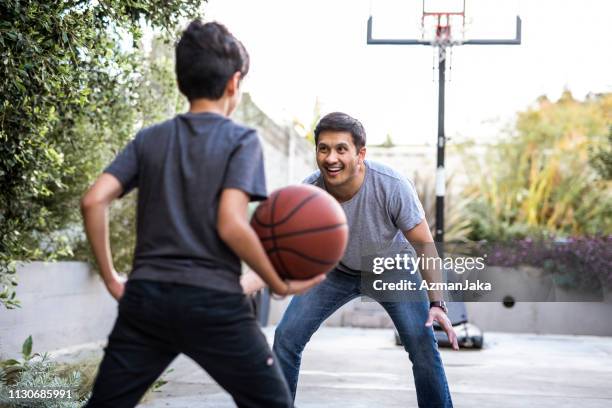 padre e hijo hispanos jugando baloncesto en el patio trasero - drive ball sports fotografías e imágenes de stock