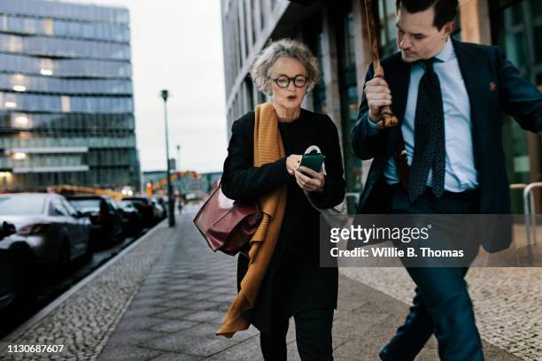 businesswoman and assistant walking down street - holding umbrella stock pictures, royalty-free photos & images