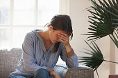 Upset depressed woman feeling tired having headache sitting on couch