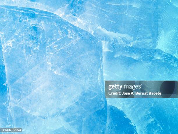 full frame of the textures formed of a block of cracked ice on a light blue color background. - glace photos et images de collection