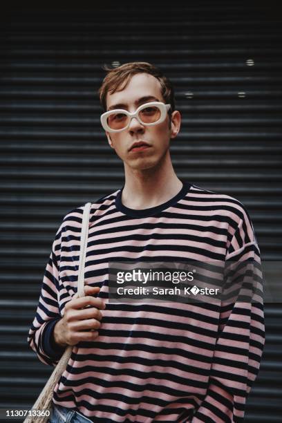 portrait of young man wearing sunglasses while standing against shutter - menswear stock-fotos und bilder