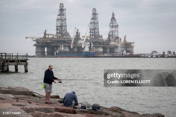 People fish in front of defunct oil drilling rigs in the Corpus Christi Ship Channel at Aransas Pass on March 11 in Port Aransas, Texas. - To realize...