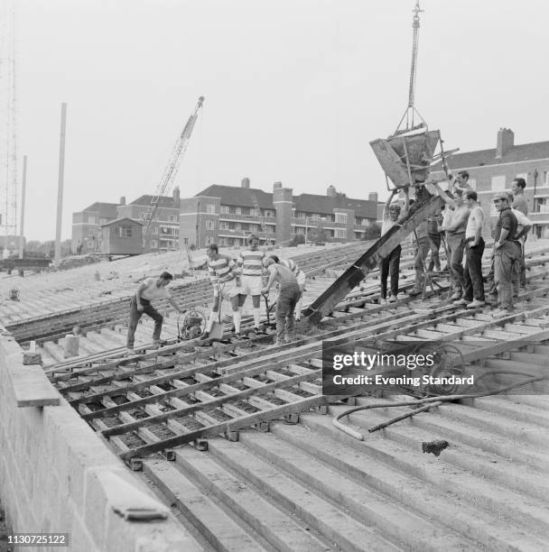 British soccer player of Queens Park Rangers Mick McGovern, Frank Clarke, and Bobby Ketch helping builders with the construction of a new stand at...