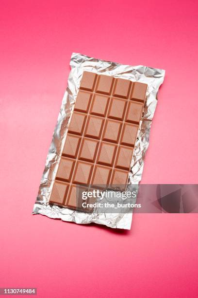 high angle view of chocolate bar on foil and pink background - ungesund leben stock-fotos und bilder