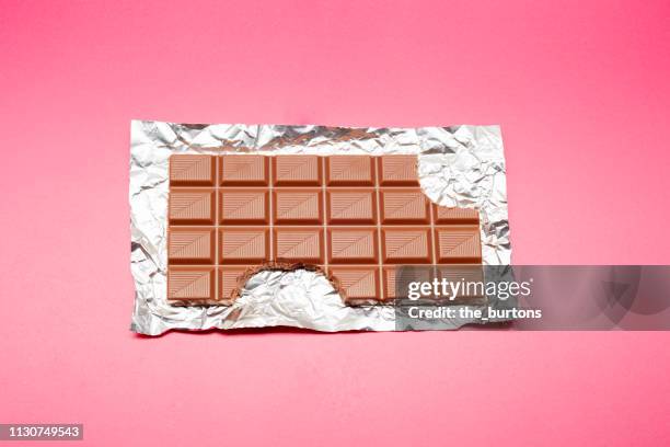 high angle view of chocolate bar on foil and pink background - schlechte angewohnheit stock-fotos und bilder