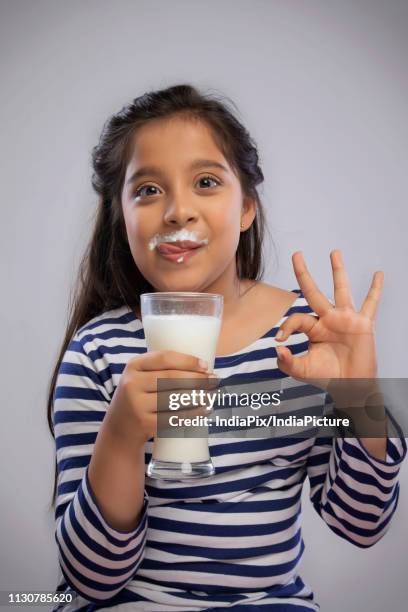 portrait of a smiling girl with milk moustache holding a glass of milk and making a ok sign with hand - girl milk moustache stock pictures, royalty-free photos & images