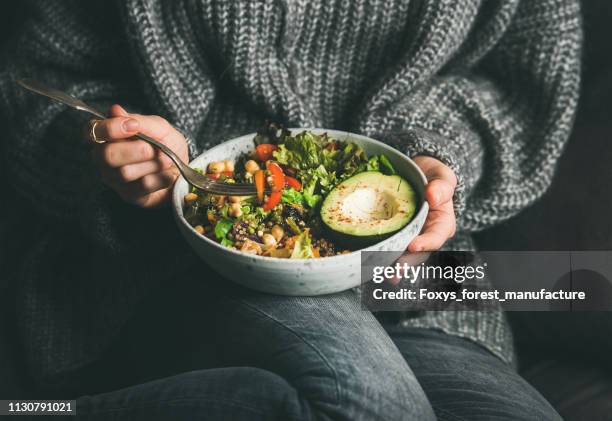 Woman in sweater eating fresh salad, avocado, beans and vegetables
