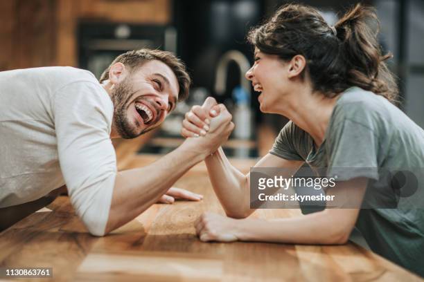 joven feliz pareja divirtiéndose mientras lucha de brazos en casa. - echar un pulso fotografías e imágenes de stock