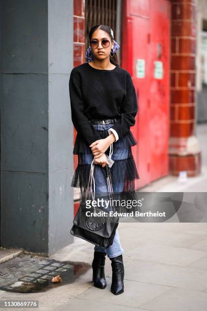 Guest wears sunglasses, a black sweater, a black handbag, black pointy boots, blue jeans under a black tulle frilly skirt, during London Fashion Week...