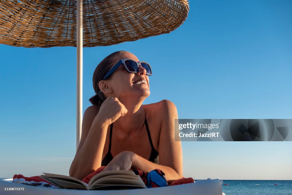 Schöne Frau liest Buch auf dem Liegen am Strand