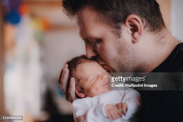 a young father holding a newborn baby son at home, kissing. - father holding sleeping baby imagens e fotografias de stock