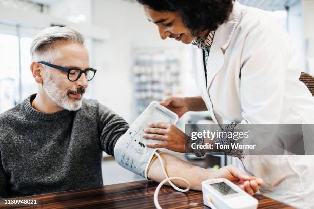 pharmacist measuring mature man's blood pressure - indicador de presión sanguínea fotografías e imágenes de stock