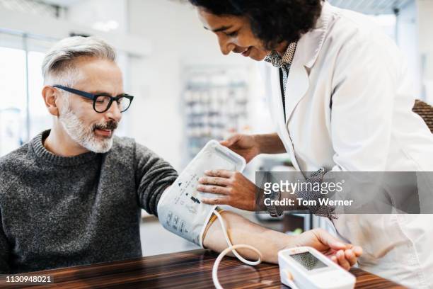 pharmacist measuring mature man's blood pressure - high blood pressure stock pictures, royalty-free photos & images