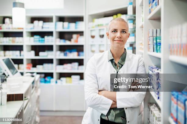 portrait of pharmacist leaning on shelves - apothekerin stock-fotos und bilder
