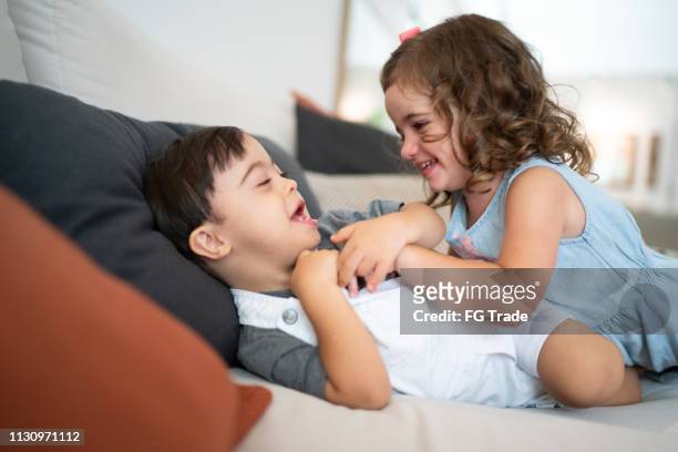 twin sibling (down syndrome brother and sister) tickling at sofa - sibling stock pictures, royalty-free photos & images
