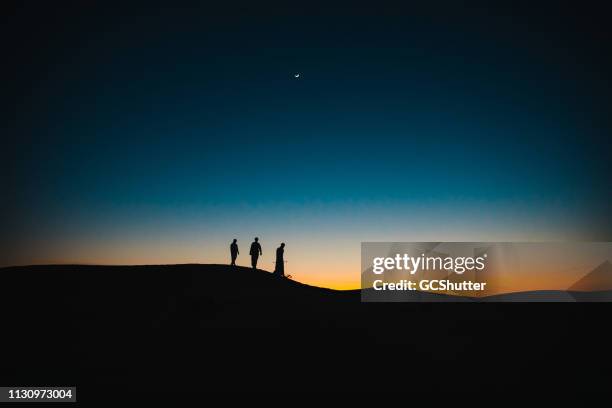arabs on the sand dunes walking behind each other during twilight - middle east people stock pictures, royalty-free photos & images