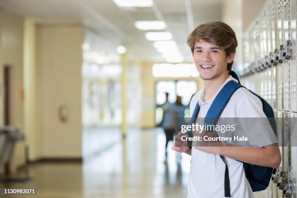 high school senior boy smiles while standing near locker and wearing backpack - kid leaning stock pictures, royalty-free photos & images