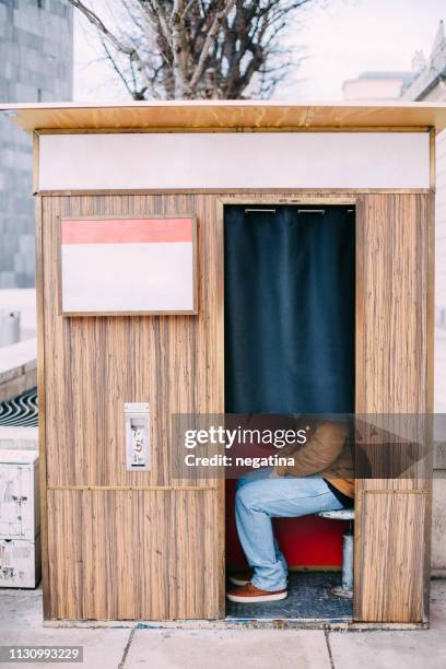 young man sits in the photobooth, face hidden by the curtain - fotobooth stock-fotos und bilder