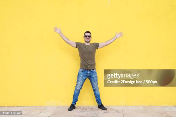 man wearing sunglasses and posing against a yellow wall - legs spread stock-fotos und bilder