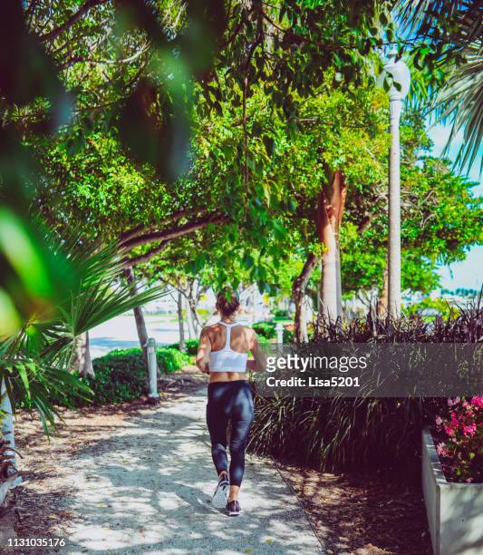 donna che corre per fare esercizio fisico lungo un sentiero ombreggiato in una città urbana, fogliame - west palm beach foto e immagini stock
